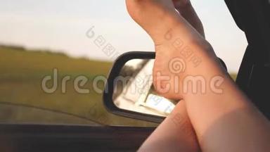 赤脚的女孩在车窗里，刺眼的阳光，骑着一辆车在路上。 女人开车旅行。 年轻女子